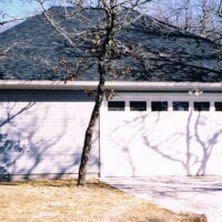 A white garage with a closed door, surrounded by leafless trees casting shadows on the building.
