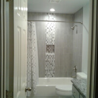 A bathroom with a bathtub, patterned shower curtain, gray tiled walls, and a granite countertop sink.