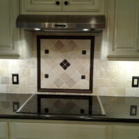 A modern kitchen backsplash with beige tiles, a black bordered tile accent, and an electric cooktop below a range hood.
