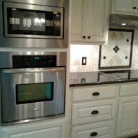 Stainless steel microwave and oven built into white cabinetry beside a tiled backsplash and black countertop.