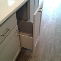 A white kitchen cabinet with a drawer and a door both open, revealing empty storage space inside.