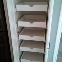 A tall cabinet with five empty white pull-out shelves is shown open next to a refrigerator in a kitchen.