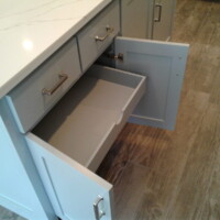 Open kitchen cabinet with an inner drawer and two smaller drawers above, all empty, on a wood floor.