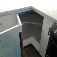 White corner kitchen cabinet with an open door showing empty shelves inside, next to a stove.