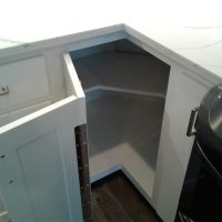 User comments White corner kitchen cabinet with an open door showing empty shelves inside, next to a stove.