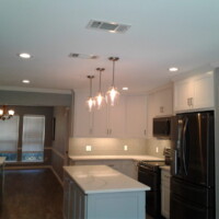 Modern kitchen with white cabinets, black appliances, pendant lights, and a central island under recessed ceiling lights.
