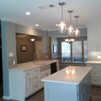 Modern kitchen with white cabinets, marble countertops, pendant lights, and stainless steel fixtures.