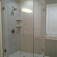Glass-enclosed walk-in shower with a wall-mounted showerhead, shelves, and a window with blinds nearby.