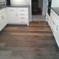 Modern kitchen with white cabinets, dark countertops, stainless appliances, and wood-look tile flooring.
