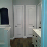 A bathroom with two white doors, a vanity with a sink and drawers, and wood-look tile flooring.