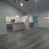 Open-concept living space with wood-look flooring, white walls, kitchen, and dining area with modern light fixtures.