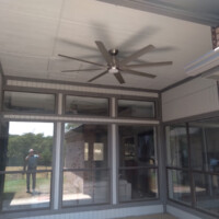Covered patio area with large ceiling fan, glass windows, and a reflection of a person taking a photo outside.