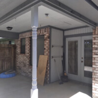 Covered outdoor patio with brick walls, a French door, cleaning tools, a dog bed, and wood leaning against the wall.