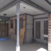 Covered outdoor patio with brick walls, a French door, cleaning tools, a dog bed, and wood leaning against the wall.