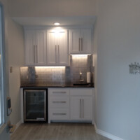 Small modern kitchenette with white cabinets, a mini fridge, silver backsplash, and wood floor.