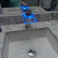 Modern bathroom faucet with blue LED lights dispenses water into a white rectangular sink on a marbled countertop.