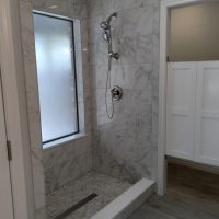 Marble-tiled walk-in shower with a frosted window, silver shower fixtures, and partial view of an adjoining room.