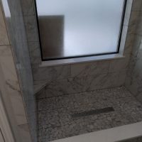 Shower with marble-patterned tile walls, mosaic tile floor, a bench, and a frosted window above a rectangular drain.