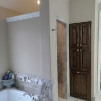 A bathroom with a bathtub, toiletries, marble tile, a wooden cabinet, and an open walk-in shower.