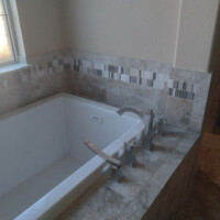 A built-in bathtub with modern fixtures and marble tile surround next to a window with decorative glass.