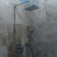 Shower with a square overhead showerhead, handheld showerhead, and beige tiled walls.