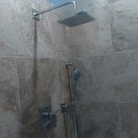 Shower with a square overhead showerhead, handheld showerhead, and beige tiled walls.