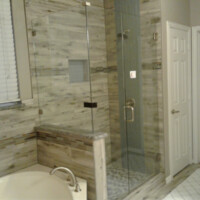 Modern bathroom with a glass-enclosed shower, tiled walls, soaking tub, and two white doors in the background.
