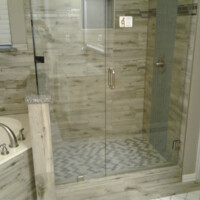 Glass-enclosed shower next to a bathtub with tile walls and a patterned tile floor in a modern bathroom.