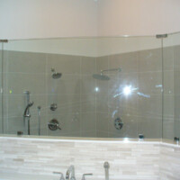 Modern bathroom shower with glass enclosure, tiled walls, and multiple showerheads above a bathtub.