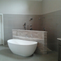 Modern bathroom with a freestanding white tub, tiled wall, open shower area, and a closed white door.