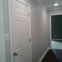 User comments A white door in a gray hallway with dark wood floors, leading to a carpeted room with a dark accent wall.