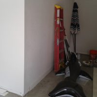 User comments A red ladder, a closed umbrella, an inflatable orca, and buckets are in the corner of a garage with some boards on the floor.
