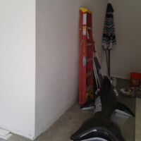 User comments A red ladder, a closed umbrella, an inflatable orca, and buckets are in the corner of a garage with some boards on the floor.