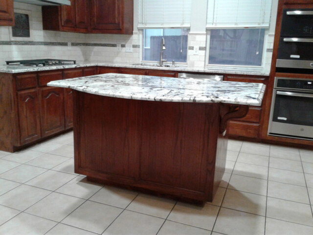 Kitchen with a marble-topped island, wooden cabinets, tiled floor, and stainless steel appliances.