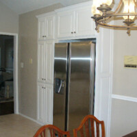 Stainless steel refrigerator set in white cabinets next to a dining table and chandelier in a kitchen.