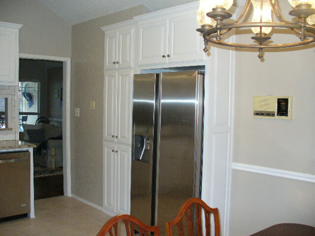 Stainless steel refrigerator built into white cabinetry in a kitchen with beige walls and a brass chandelier.