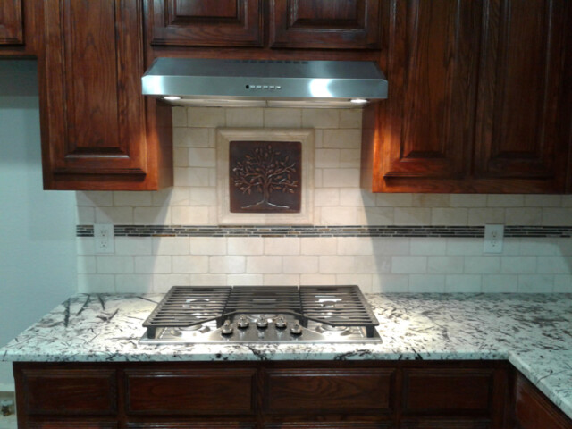 A gas cooktop with five burners is installed in a granite countertop beneath a range hood and wooden cabinets.