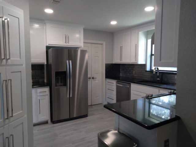 Modern kitchen with white cabinets, stainless steel appliances, black countertops, and gray tile backsplash.
