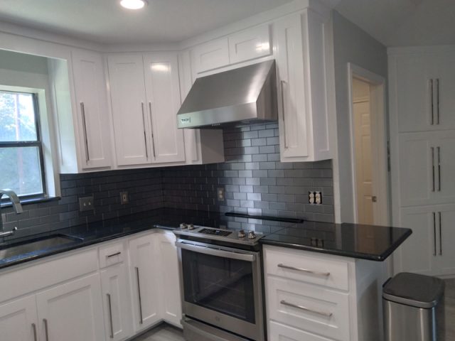 Modern kitchen with white cabinets, stainless steel appliances, black countertops, and dark gray subway tile backsplash.