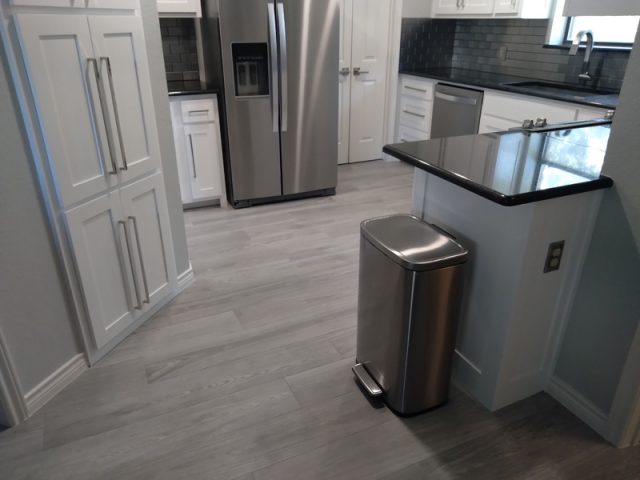 Modern kitchen with stainless steel appliances, white cabinets, light gray flooring, and a metal trash can.