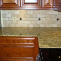 Granite kitchen countertop with wooden cabinets and light tiled backsplash featuring small dark square accents.