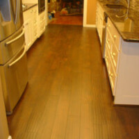 A kitchen with dark wood flooring, white cabinets, stainless steel refrigerator, and granite countertops.