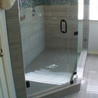 Modern glass-enclosed shower with gray tiles, black fixtures, and natural light from two windows.