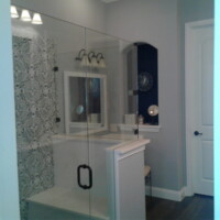 Modern bathroom with glass shower enclosure, patterned shower curtain, and a vanity with a mirror and light fixture.