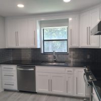 Modern kitchen with white cabinets, black countertops, stainless steel appliances, and a window above the sink.