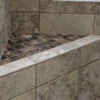 A tiled corner shower bench with a dark mosaic top and tan stone tile sides and walls.
