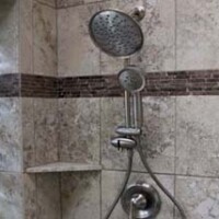 Tile shower with two shower heads, a handheld spray, and a small corner shelf.