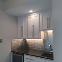 Modern kitchen corner with white cabinets, stainless steel subway tile backsplash, and black countertop.