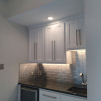 Modern kitchen corner with white cabinets, stainless steel subway tile backsplash, and black countertop.